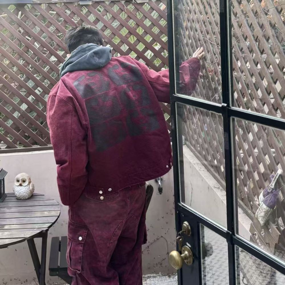 Person in a maroon outfit opening a glass door with a lattice fence in the background.
