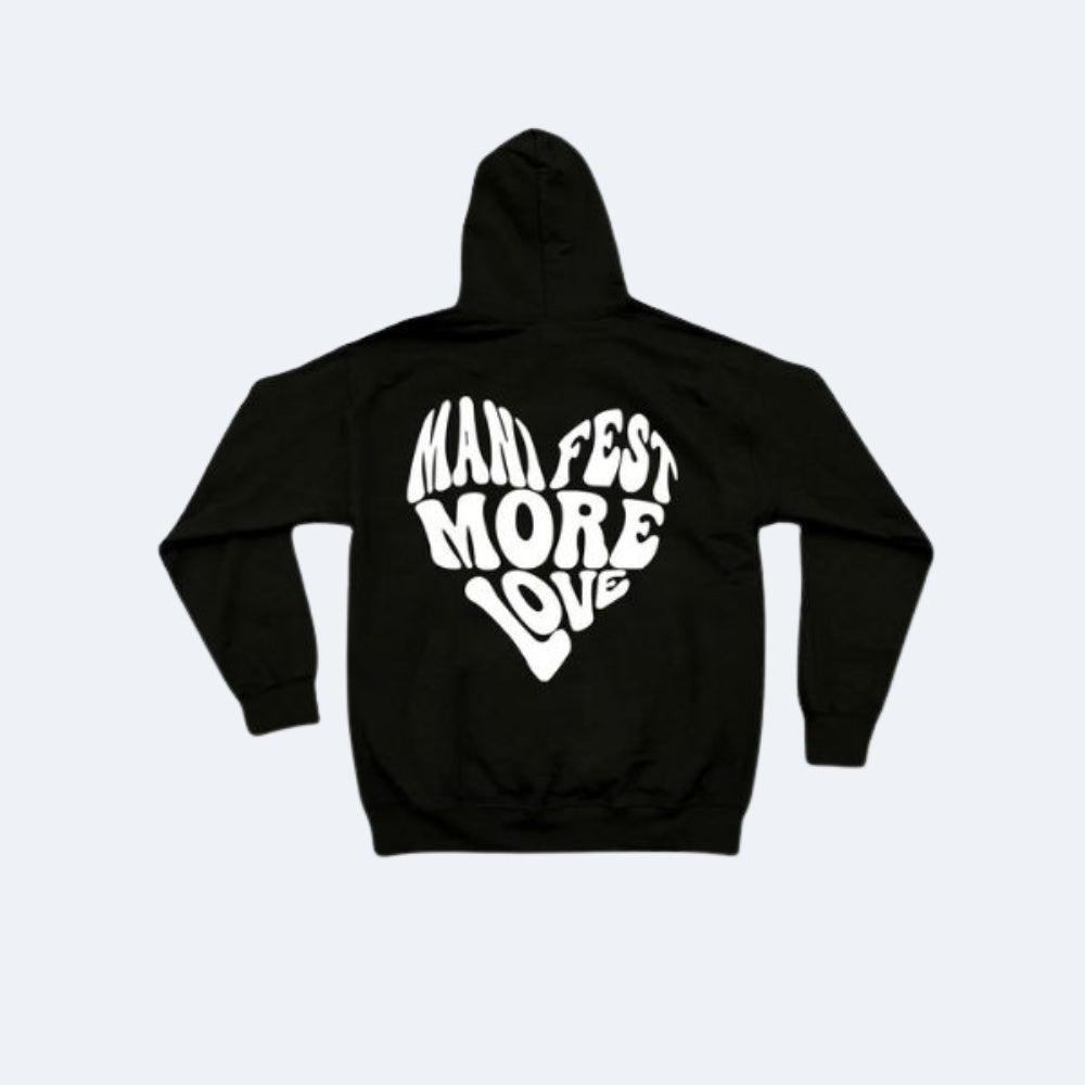 Black. A black pullover hoodie shown from the back, featuring a large white graphic text that reads MANIFEST MORE LOVE in a stylized heart-like shape.