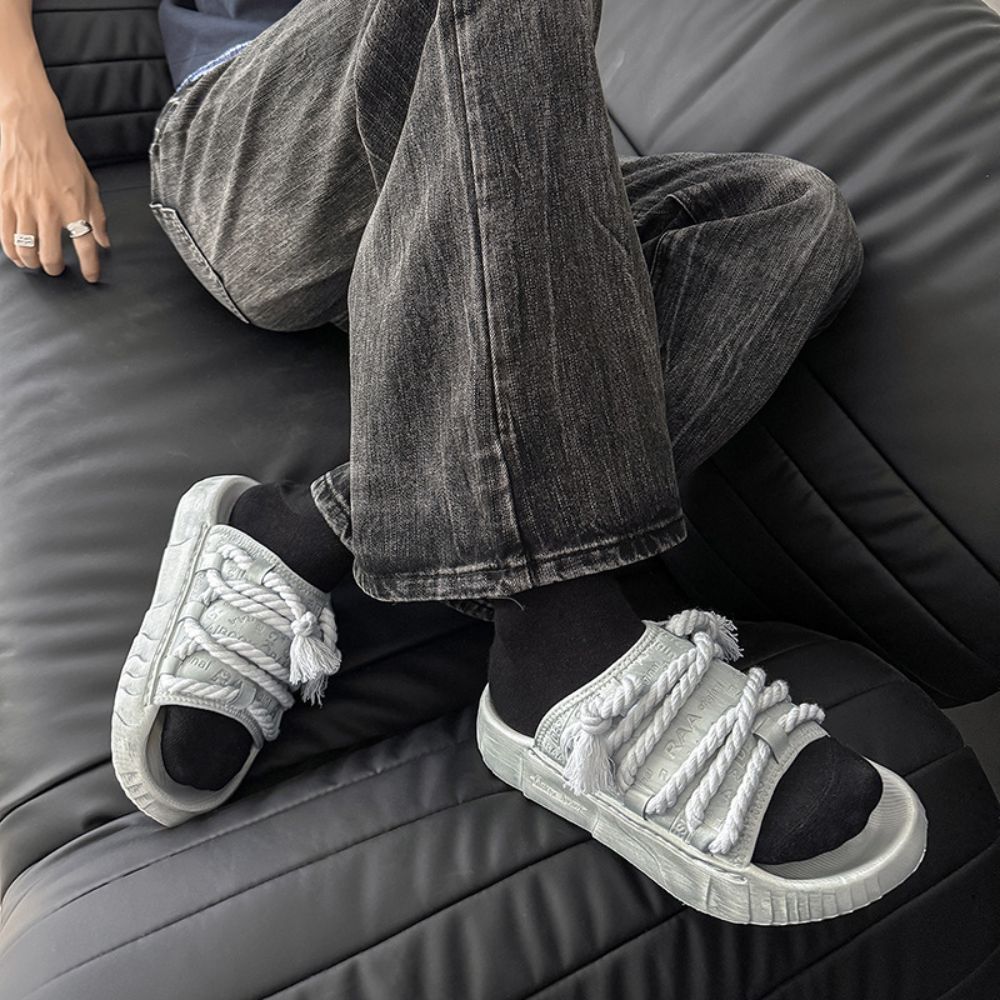 Person wearing white sneakers with braided details sitting on a gray couch.