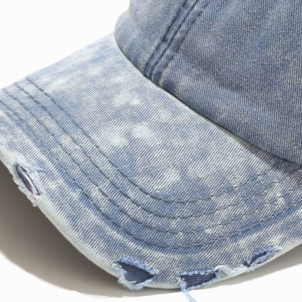 Close-up of a denim cap with frayed edges on a light gray background