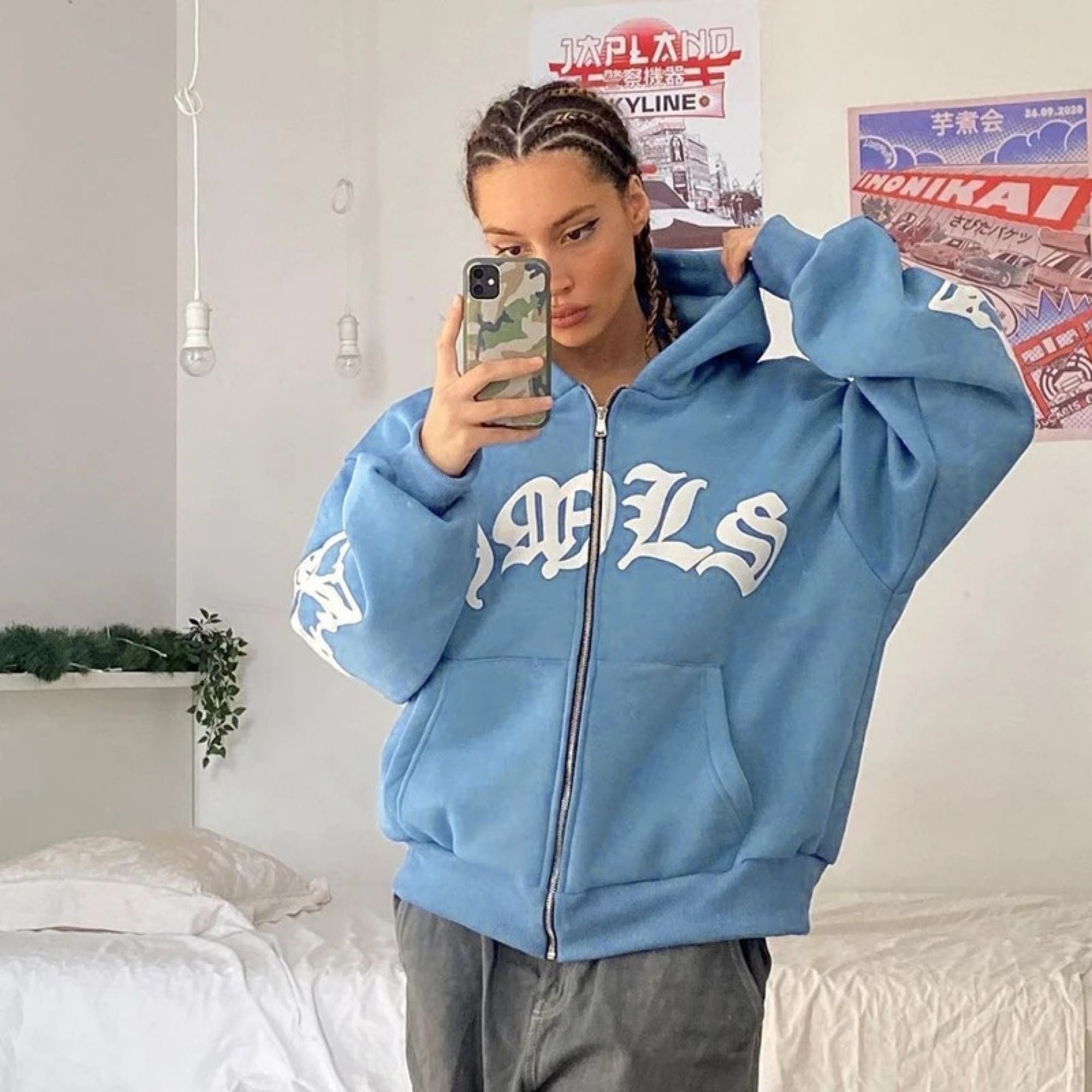 Person wearing a blue hoodie with 'GRLS' text, taking a mirror selfie in a bedroom.