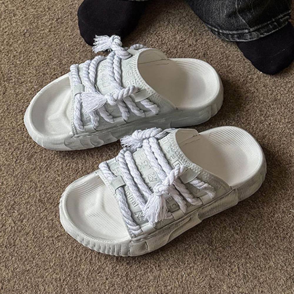 White slides with braided straps on a carpeted floor