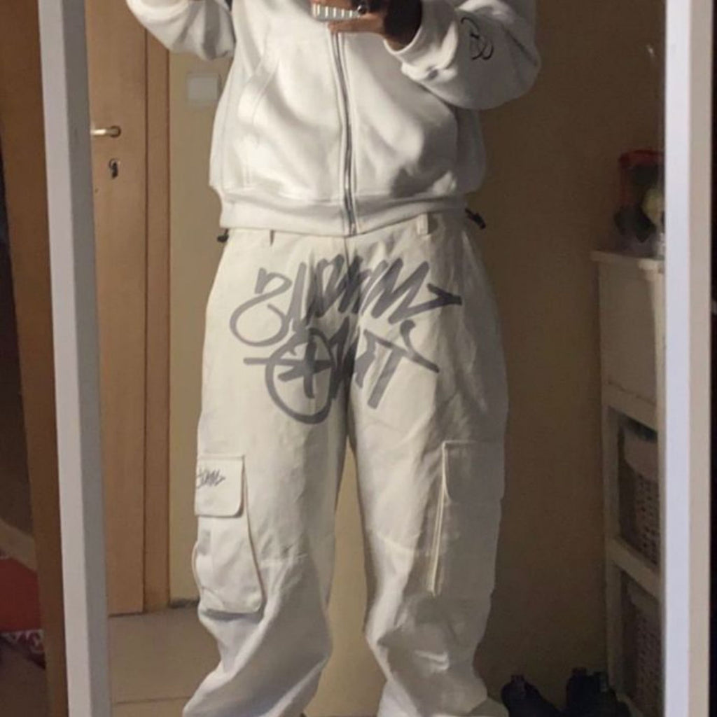 Person wearing a light gray tracksuit with branding in a room.