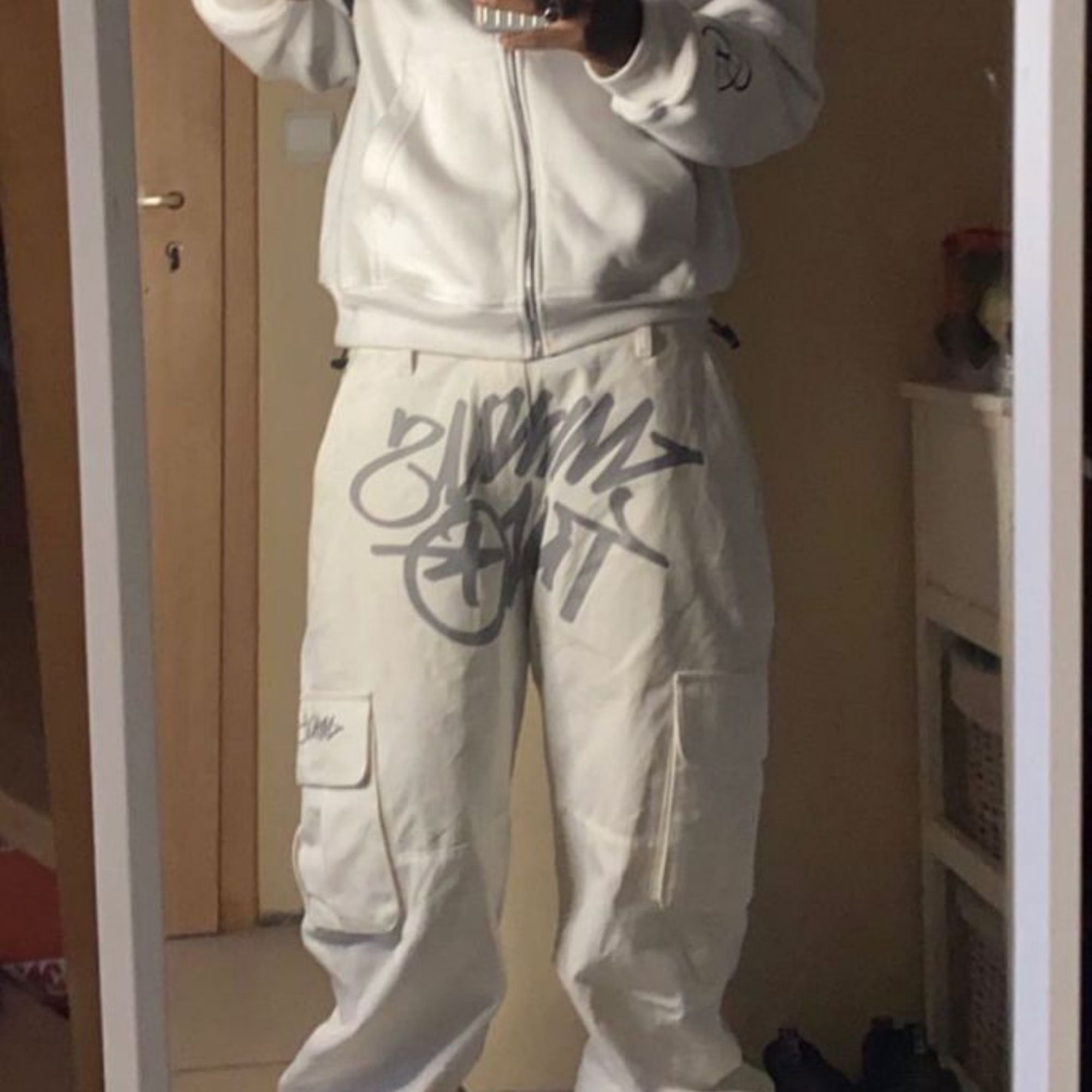 Person wearing a light gray tracksuit with branding in a room.