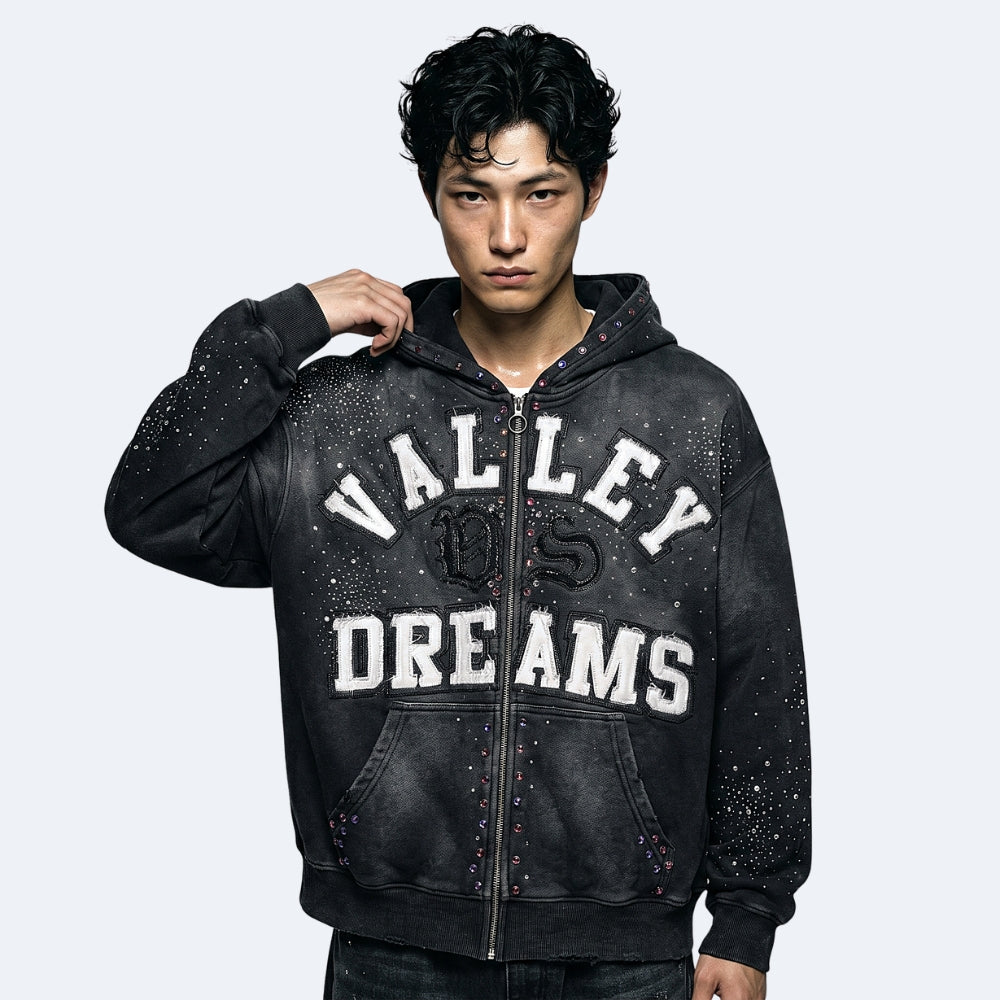 Black. A man wearing a black distressed zip-up hoodie with VALLEY DREAMS printed in white varsity-style letters on the front.