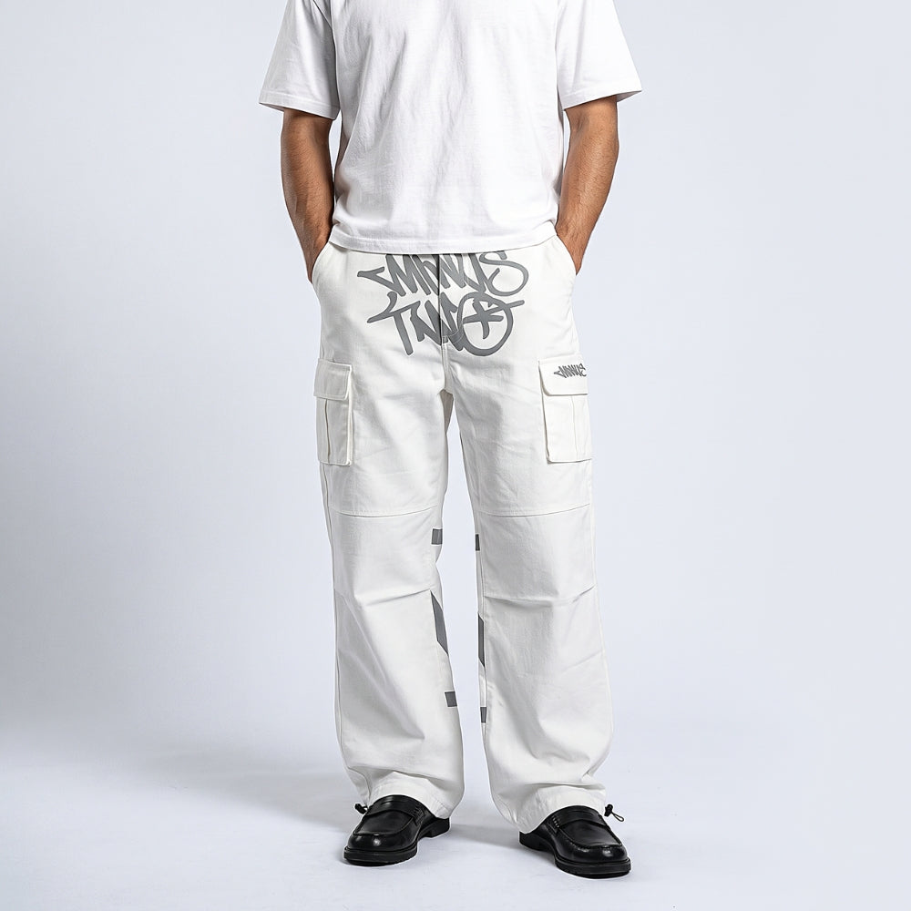 A person wearing off-white cargo pants with a large gray graphic print on the left thigh and a small logo on the right pocket, paired with a white t-shirt and black loafers, shown from the chest down against a light gray studio background.