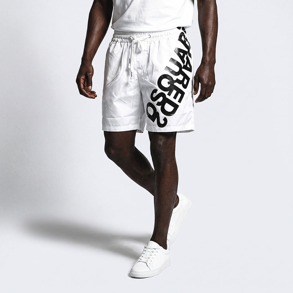 White. A model wearing white drawstring shorts with a large black diagonal logo print on the side, paired with a white t-shirt and white sneakers.