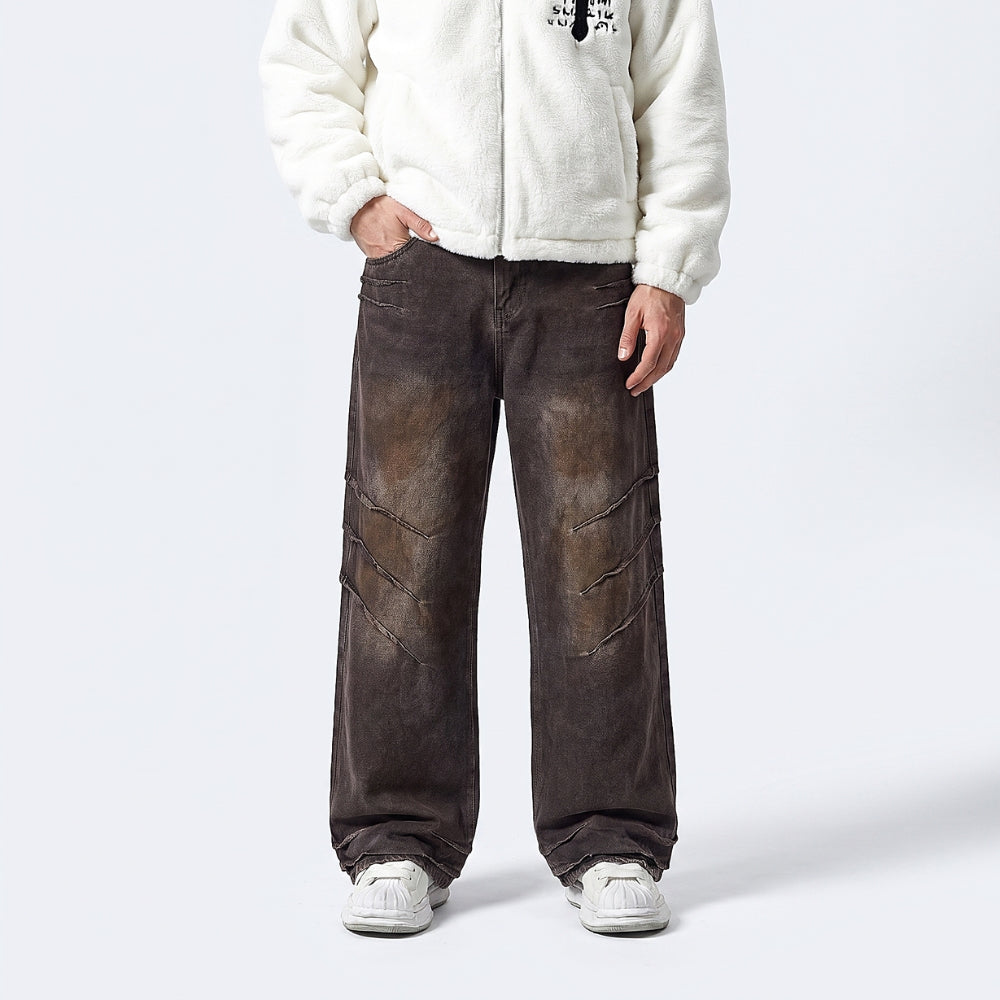 A person wearing loose, wide-leg brown distressed jeans with diagonal seam details, paired with a cream fleece jacket and white sneakers, shown from the chest down on a light gray studio background.