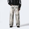 A person wearing wide-leg jeans with a gray and white marble or tie-dye pattern, styled with a black jacket and black shoes, against a light gray studio background.