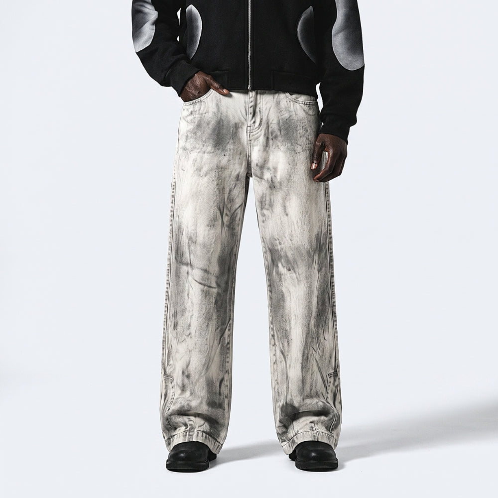 A person wearing wide-leg jeans with a gray and white marble or tie-dye pattern, styled with a black jacket and black shoes, against a light gray studio background.