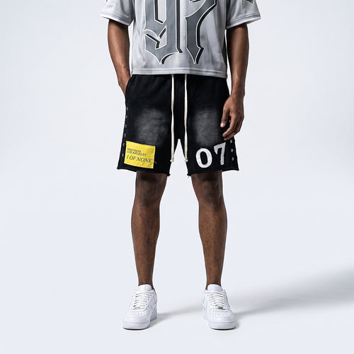 A model is shown from the waist down wearing black washed athletic shorts with white drawstrings, a yellow 'TERRITORY OF THE LAP NINE' patch on the left leg, and white sneakers, paired with a gray graphic t-shirt against a light gray studio background.