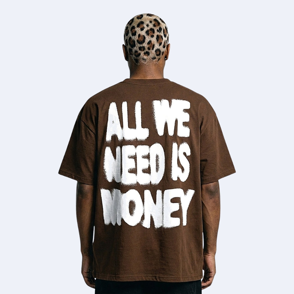 A man viewed from behind wearing a brown oversized t-shirt with the phrase 'ALL WE NEED IS MONEY' printed in large white graffiti-style letters on the back. He is also wearing a leopard-print cap, set against a solid light gray background.