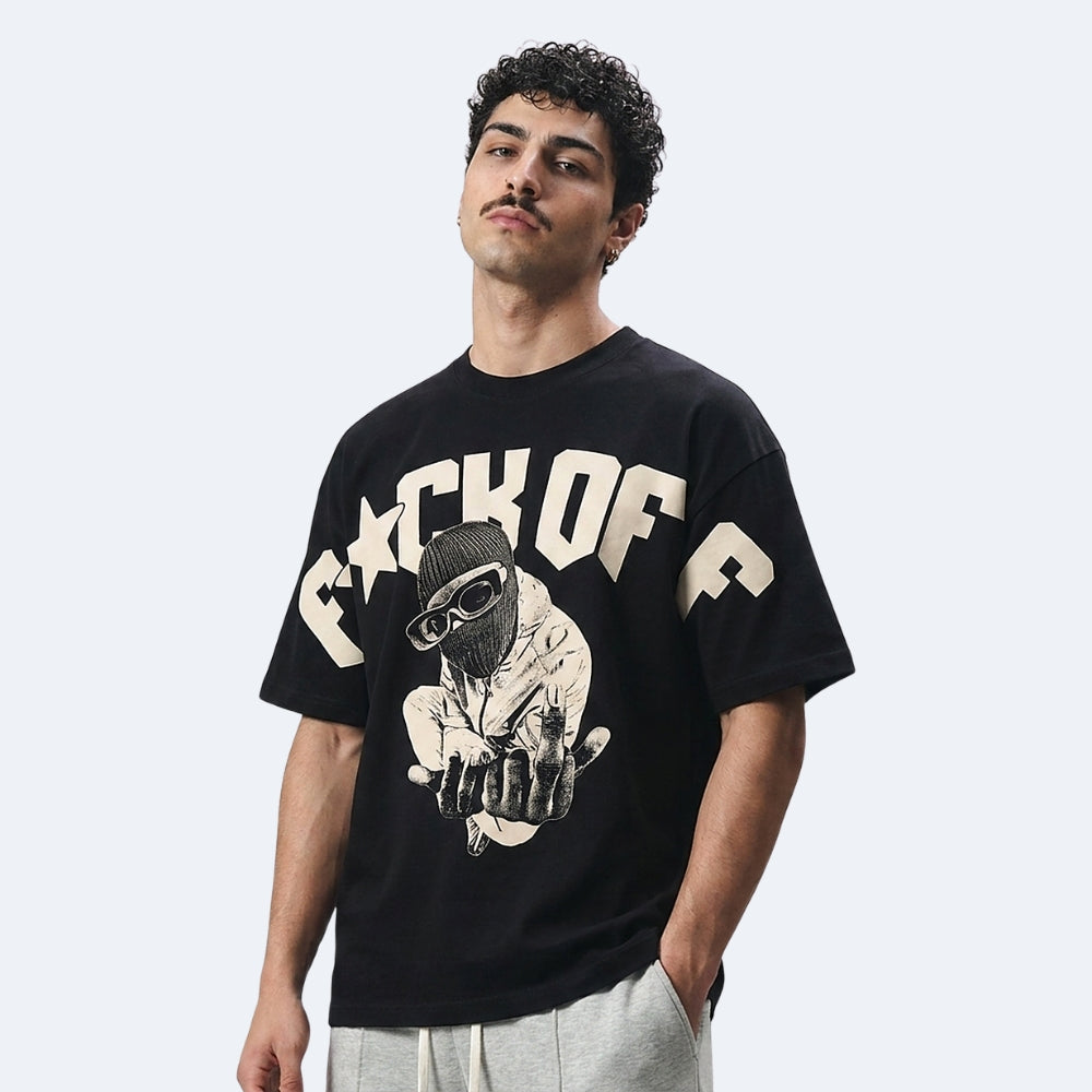 A man wearing a black oversized graphic t-shirt with a cream-colored 'CCK OF C' text and a hand graphic, paired with light gray sweatpants, against a light gray studio background.