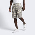 A model wearing beige and gray camouflage cargo shorts, styled with a white t-shirt and white sneakers, set against a plain light gray studio background.