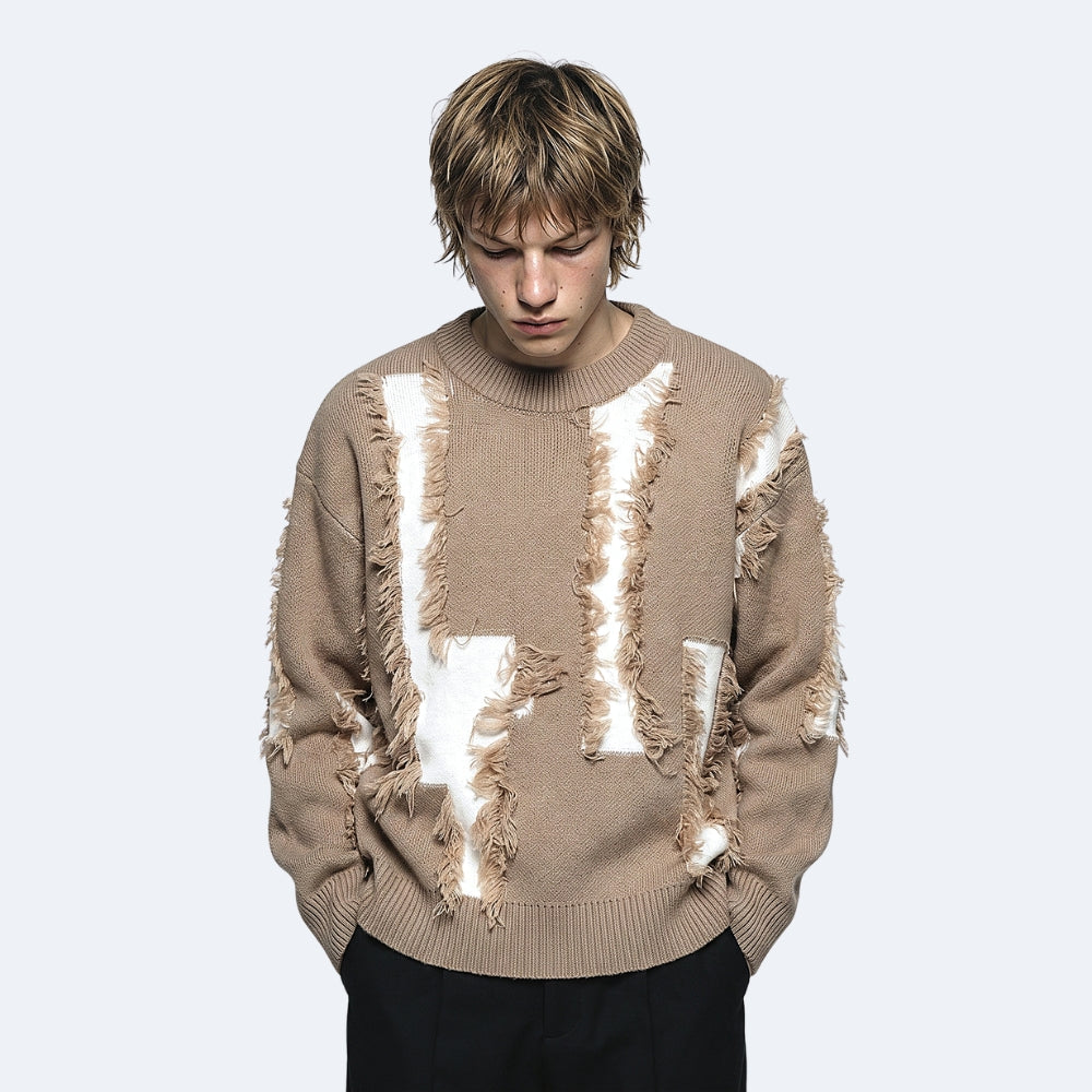 Brown. A model wearing a beige crewneck sweater with distressed, ripped details showing white lining, paired with black pants.