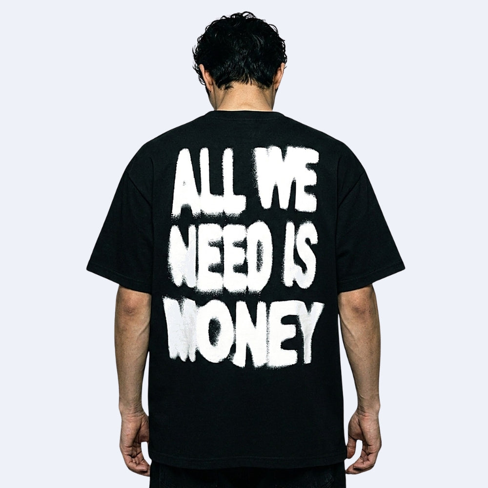 A man viewed from behind wearing a black t-shirt with the phrase 'ALL WE NEED IS MONEY' printed in a large, white, distressed graffiti-style font on the back.