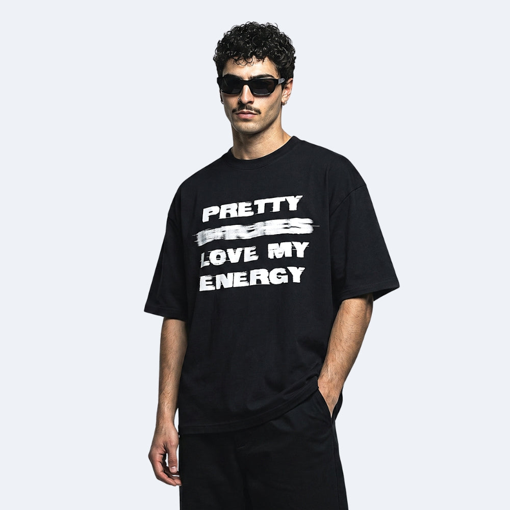 Black. A man wearing a black oversized t-shirt with text printed in white across the chest, paired with black pants and sunglasses.