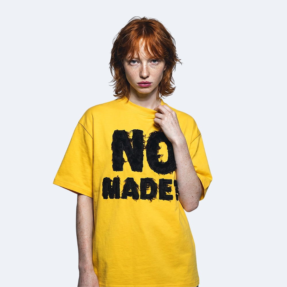 Yellow. A model wearing the KRUX No Made tee in yellow with textured lettering.