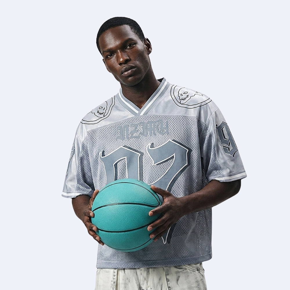 A man modeling a light gray and silver basketball jersey with the number 07 and 'NITRO' on the front, holding a teal basketball against a light gray studio background.
