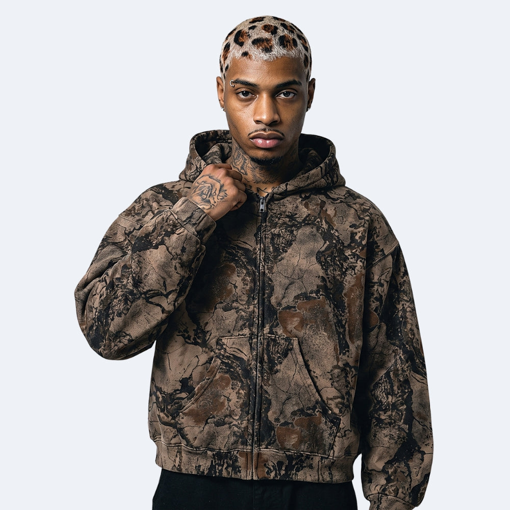 Brown. A man wearing a brown and black camouflage zip-up hoodie with a matching leopard-print hairpiece.