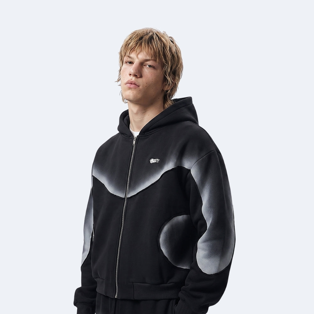A model wearing a black zip-up hoodie with a gray gradient abstract pattern on the chest and sleeves, set against a light gray studio background.