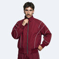 A man wearing a burgundy athletic zip-up jacket with white piping details, posed against a light gray studio background.