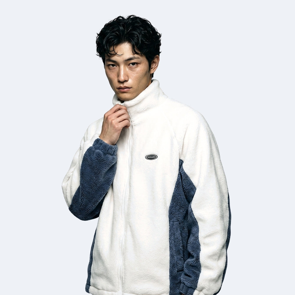 Blue. A man wearing a white and navy blue fleece zip-up jacket, posing against a light gray background.