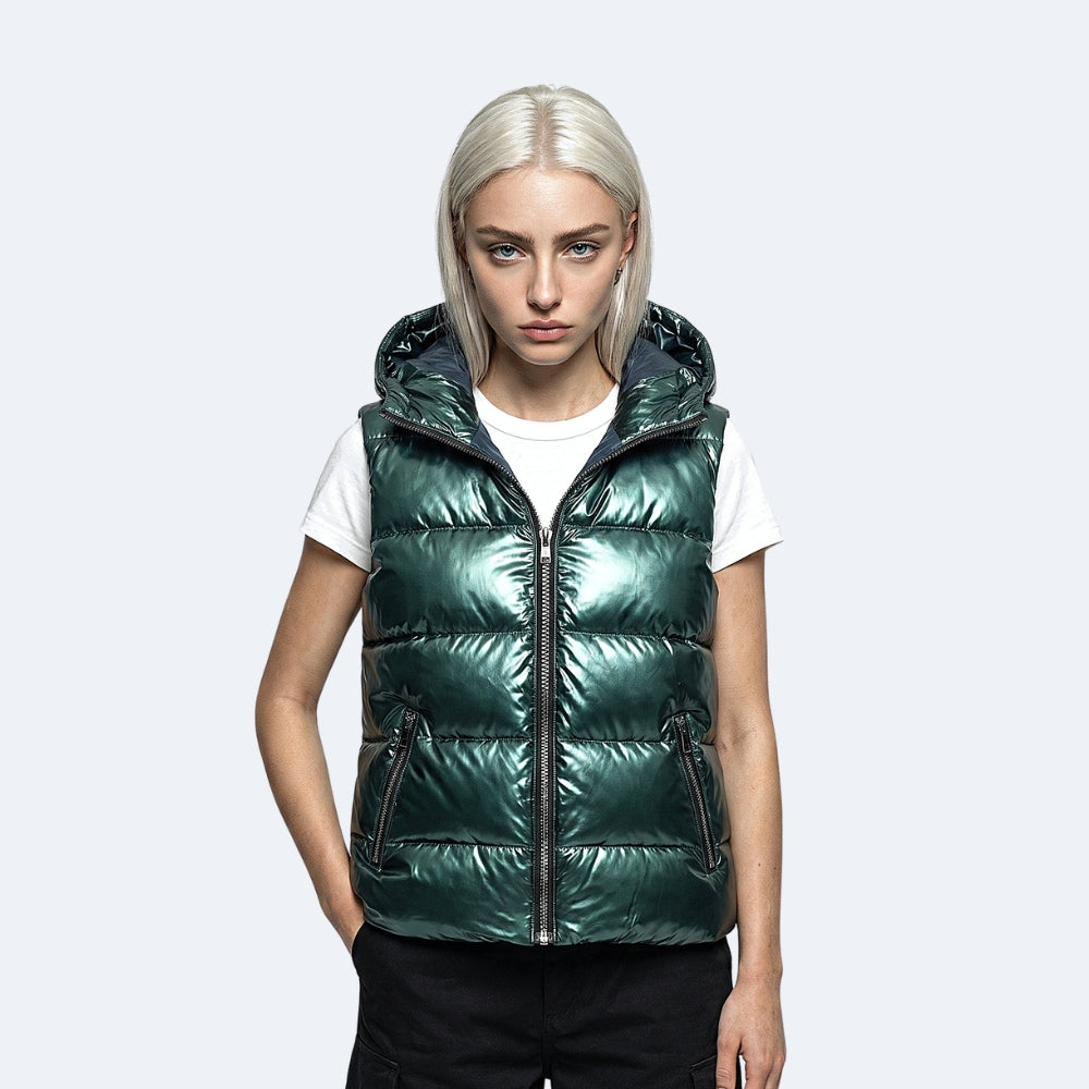Green. A model with platinum blonde hair wearing a shiny, metallic dark green hooded puffer vest over a white t-shirt and black pants.