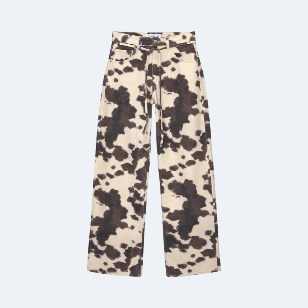 A pair of wide-leg trousers featuring a dark brown and beige cow-print pattern, displayed flat against a light gray background.