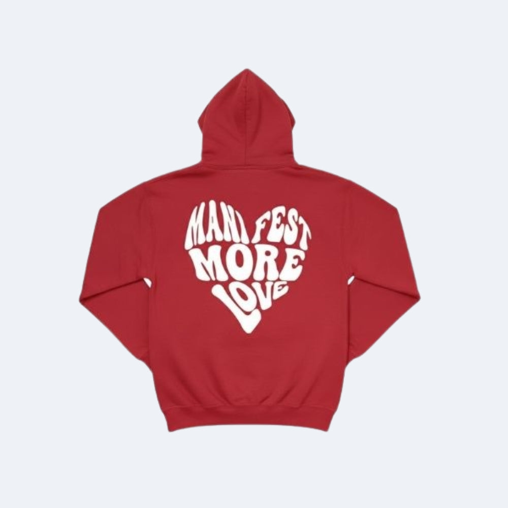 Red. A red pullover hoodie shown from the back, featuring a large white graphic text that reads MANIFEST MORE LOVE arranged in a heart shape.
