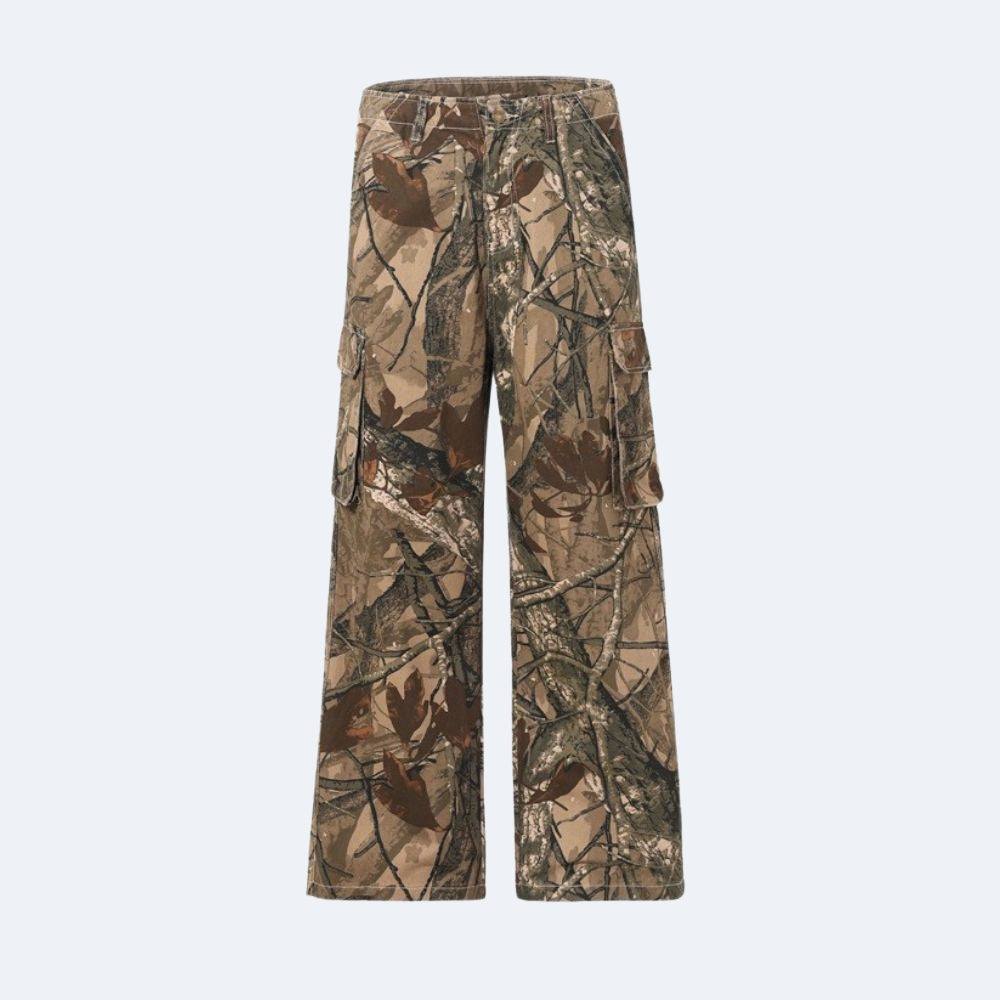 A pair of camouflage cargo pants with a realistic woodland tree branch and leaf pattern in shades of brown, tan, and green, shown against a light gray background.