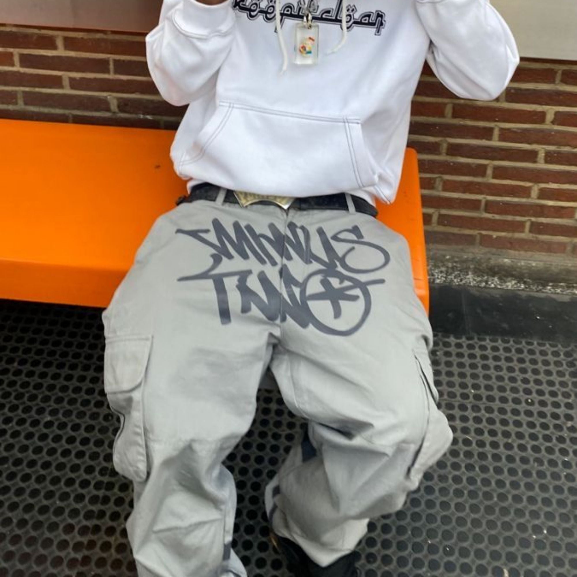 Person wearing a white hoodie and gray pants with text, sitting on an orange bench.