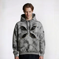 Person wearing a gray tie-dye hoodie with black leaf designs on a white background