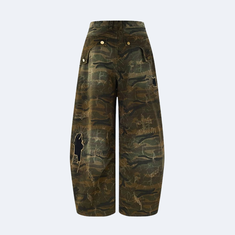 Distressed camouflage cargo pants with a high waist, featuring a green and brown camo pattern, gold-tone hardware, and a black distressed patch on the left leg.