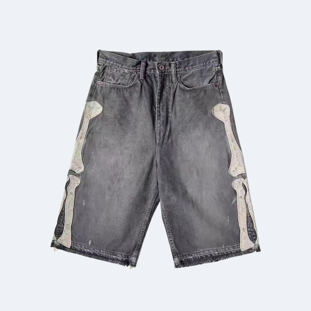 A pair of dark gray acid-wash denim shorts featuring decorative bone appliques on the outer thighs, shown flat against a light gray background.