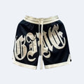 Black. Black mesh athletic shorts with a large cream-colored Gothic letter print on the front, featuring a cream drawstring and matching trim.