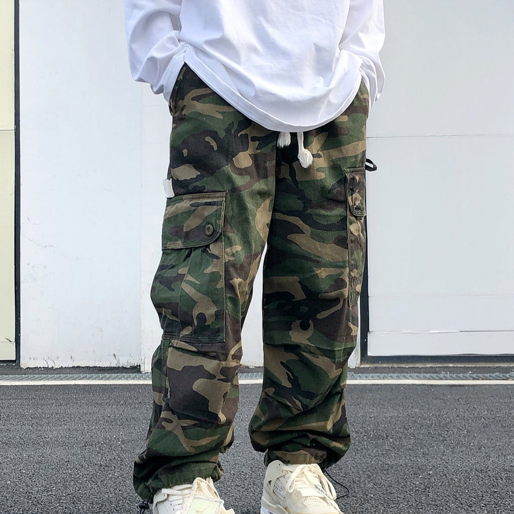 Person wearing camouflage pants and a white hoodie against a plain background