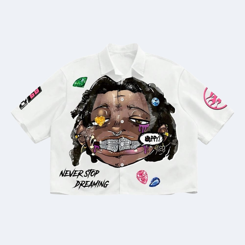 A white short-sleeve button-up shirt with a large central graphic of a smiling person with dark hair, colorful gem illustrations, and the text 'NEVER STOP DREAMING' on the front. The shirt also has small graphic prints on both sleeves, shown against a light gray background.