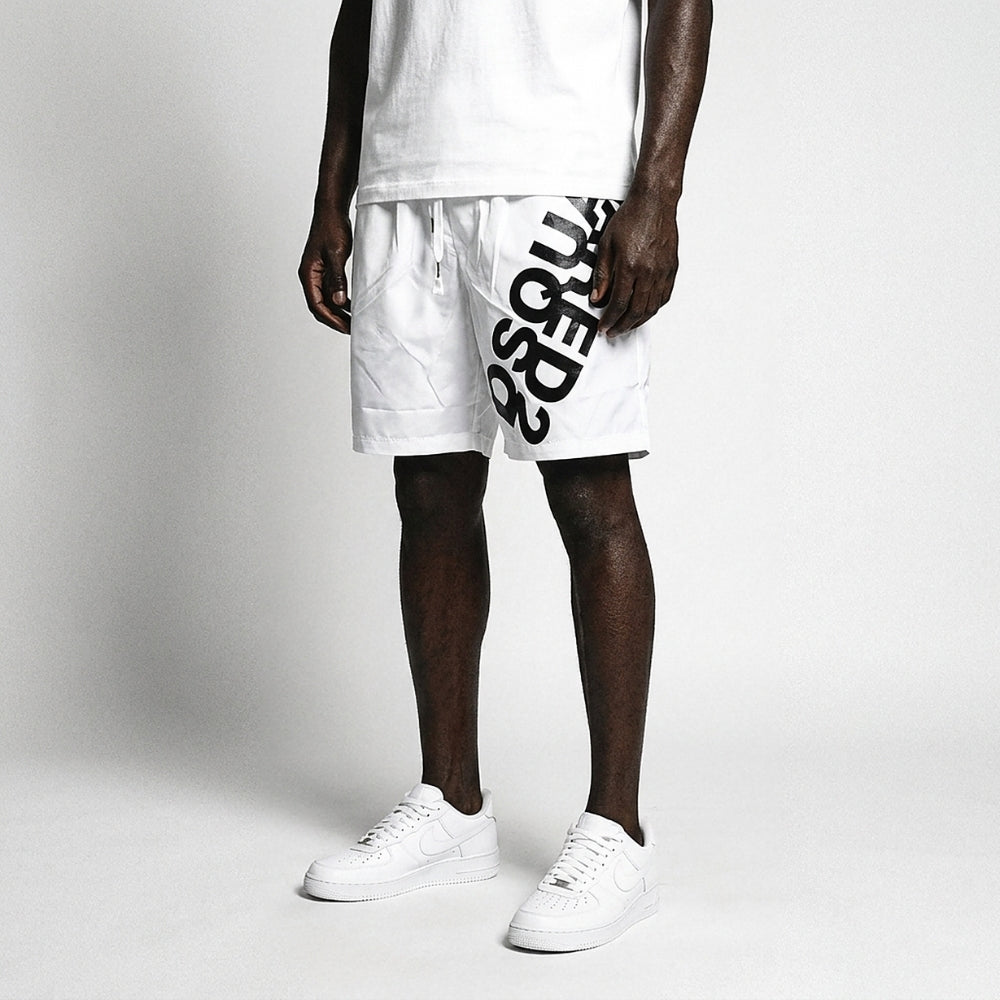 White. A model wearing white athletic shorts with a large black graphic print on the side, paired with a white t-shirt and white sneakers.
