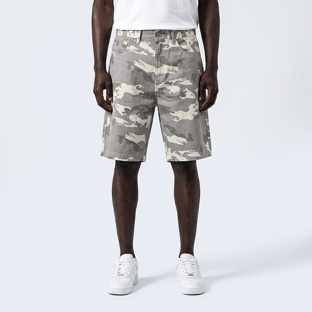 A model wearing gray and beige camouflage shorts, styled with a white t-shirt and white sneakers, photographed against a light gray studio background.