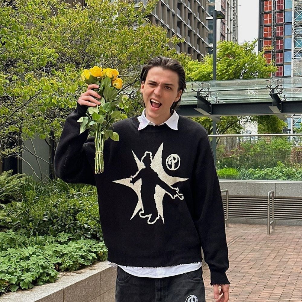 Person holding yellow flowers outdoors with a black sweater featuring a white graphic design.