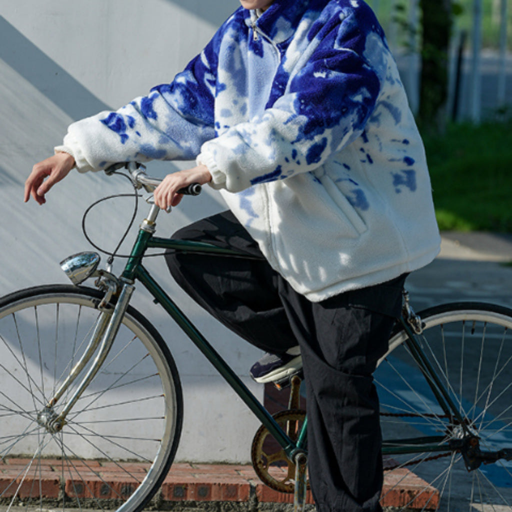 Person wearing a blue and white tie-dye jacket on a bicycle
