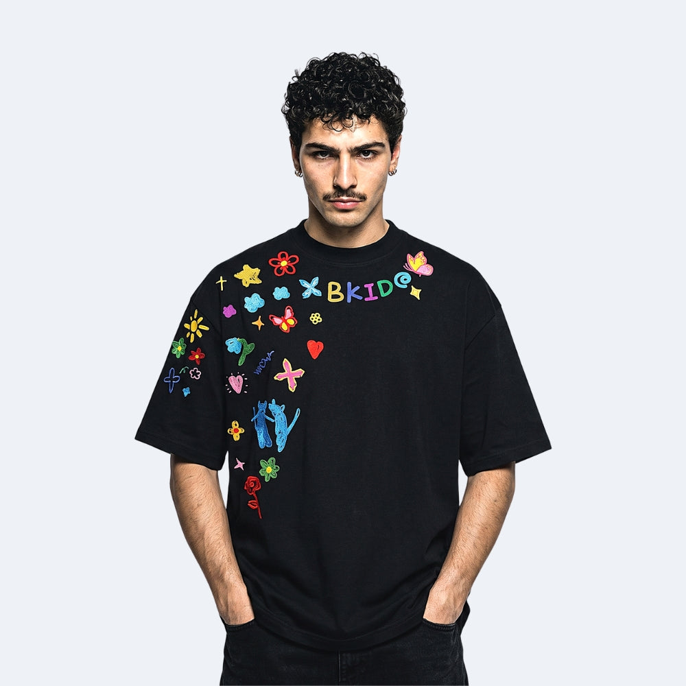 Black. A man modeling a black oversized t-shirt with colorful embroidered graphics and text on the chest.