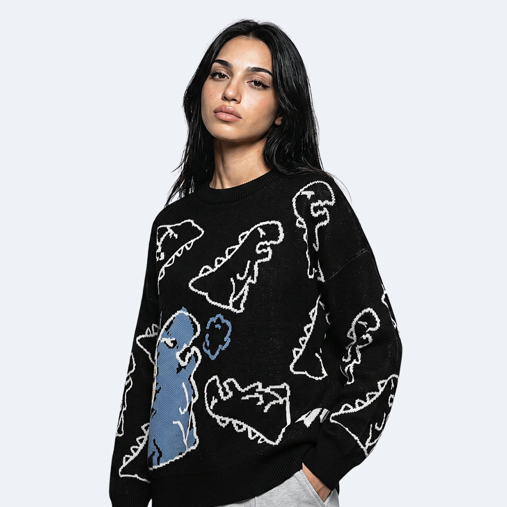 Black. A woman wearing a black crewneck sweater with a knit pattern of white and blue dinosaur silhouettes.
