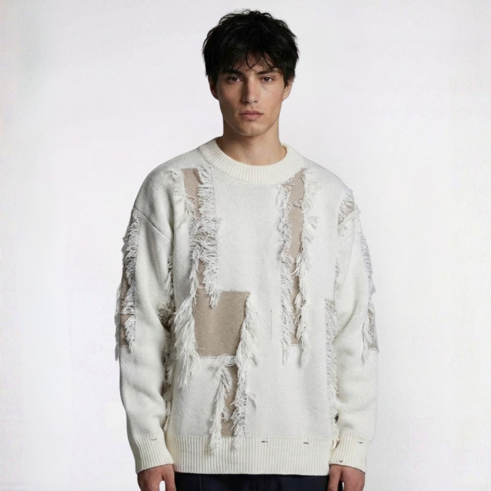 Person wearing a white sweater with fringe details on a plain background