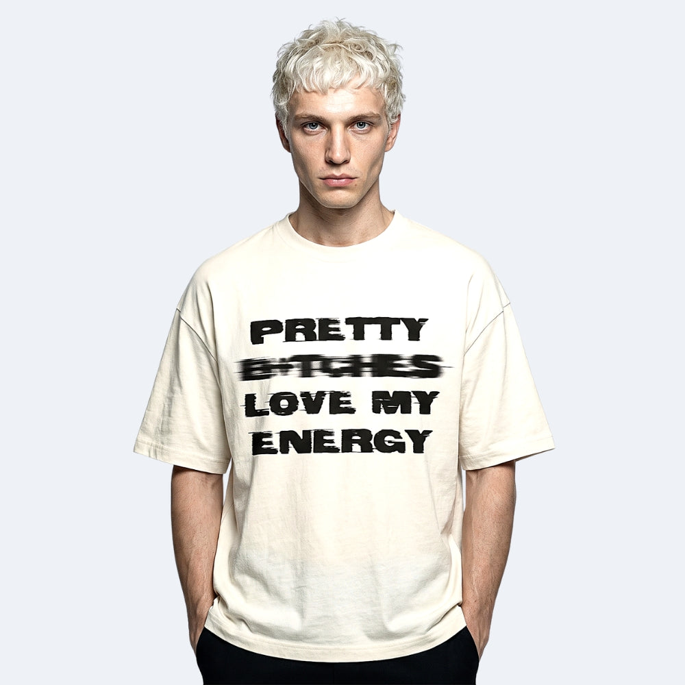 Beige. A model with platinum blonde hair wearing a cream-colored oversized t-shirt with text printed in black across the front.