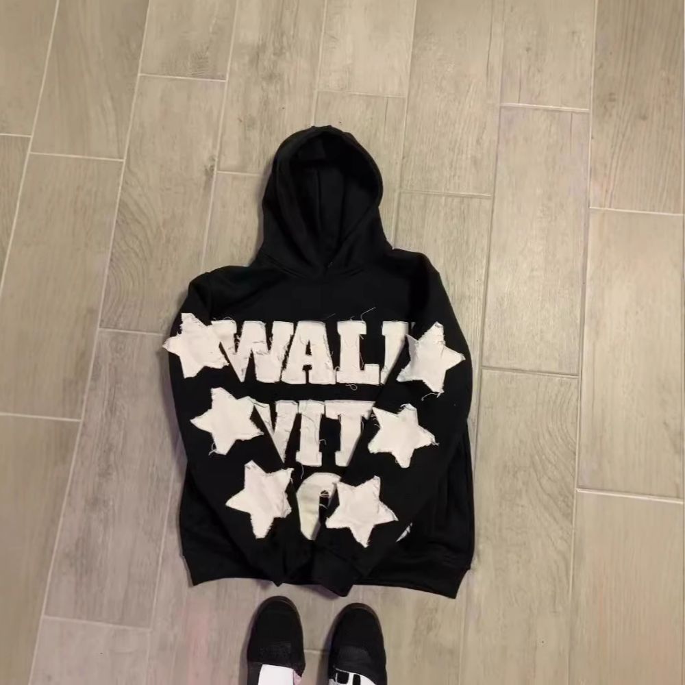 Black hoodie with white star designs and text on a wooden floor