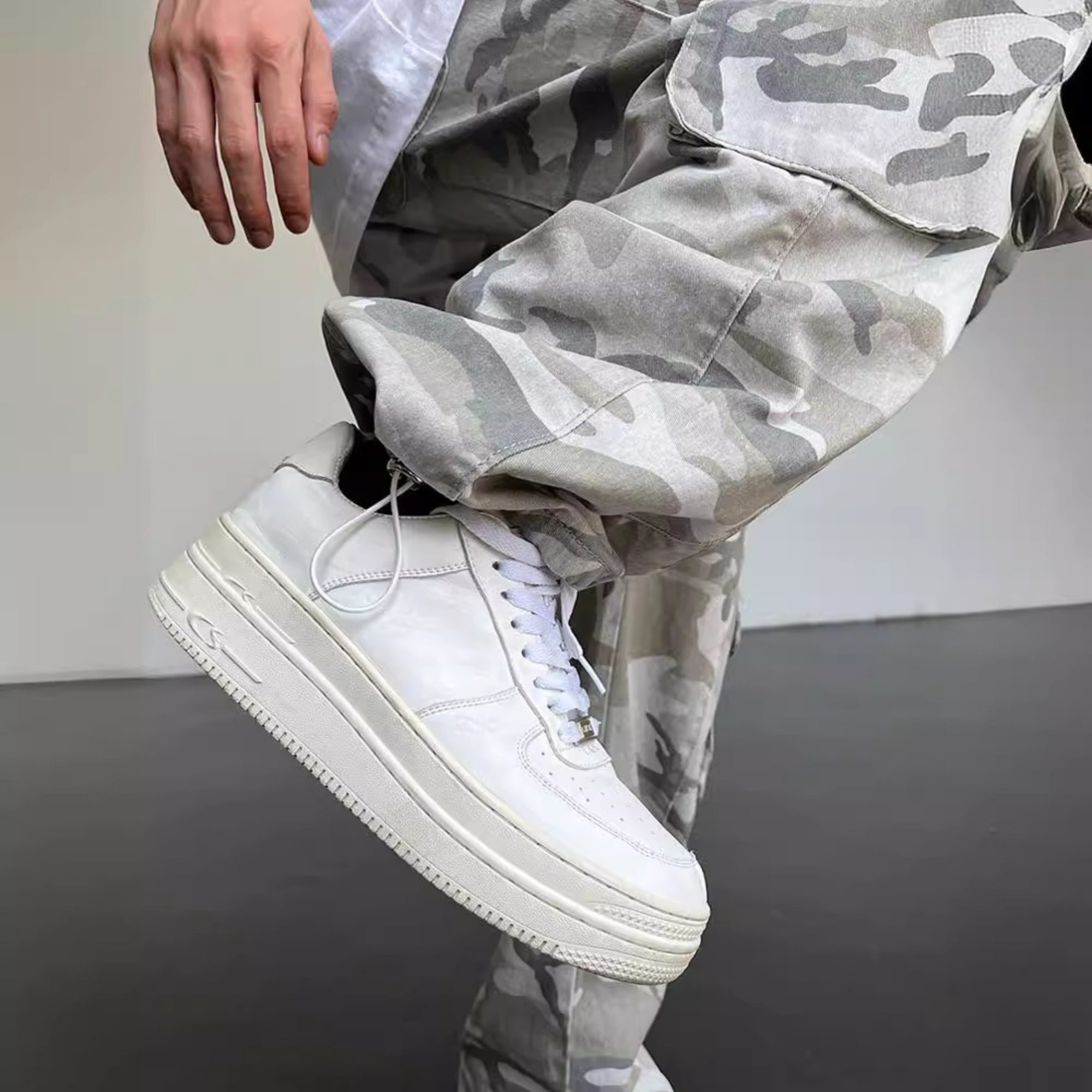 White high-top sneakers with a person wearing camouflage pants on a plain background