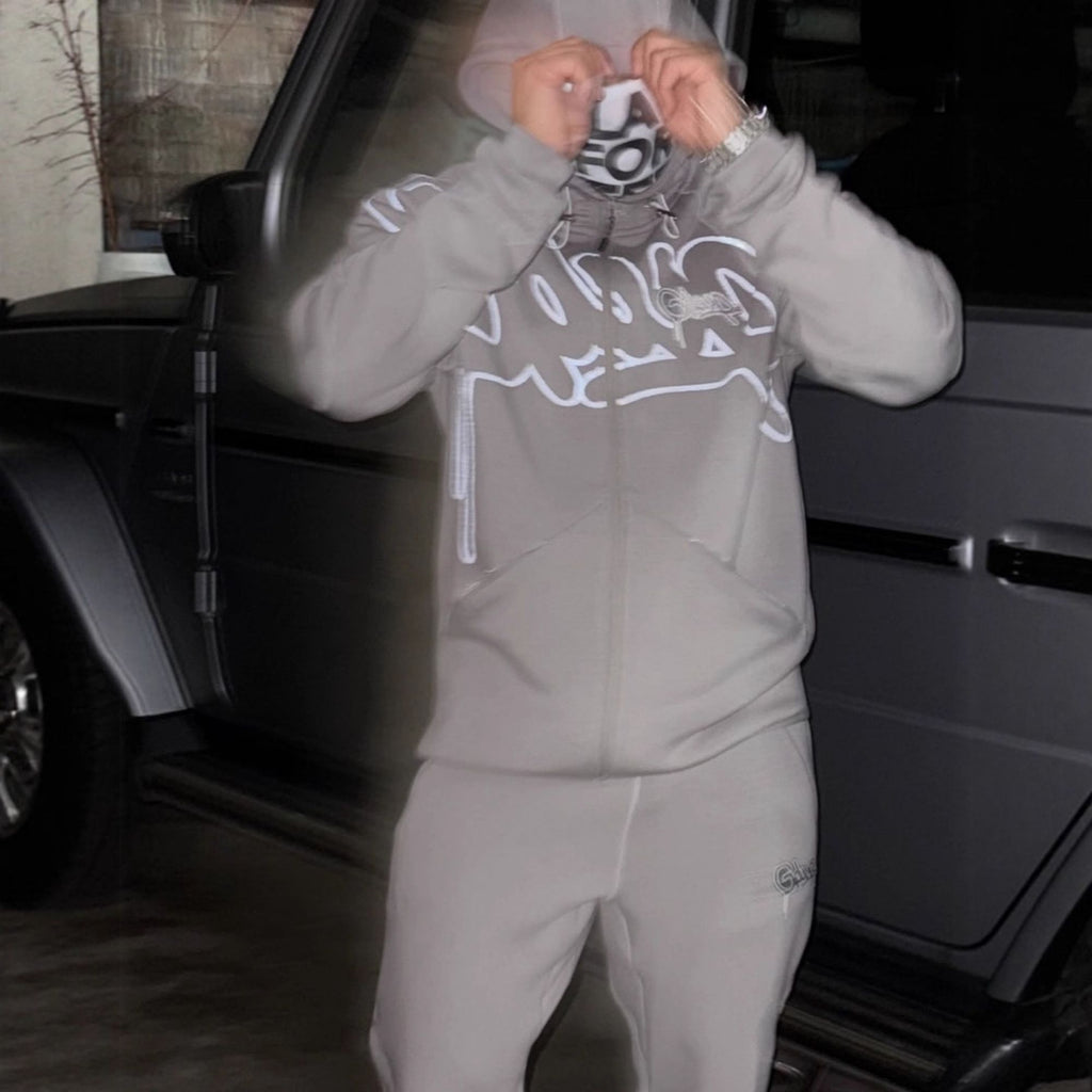 Person wearing a gray tracksuit with a logo, standing next to a car.