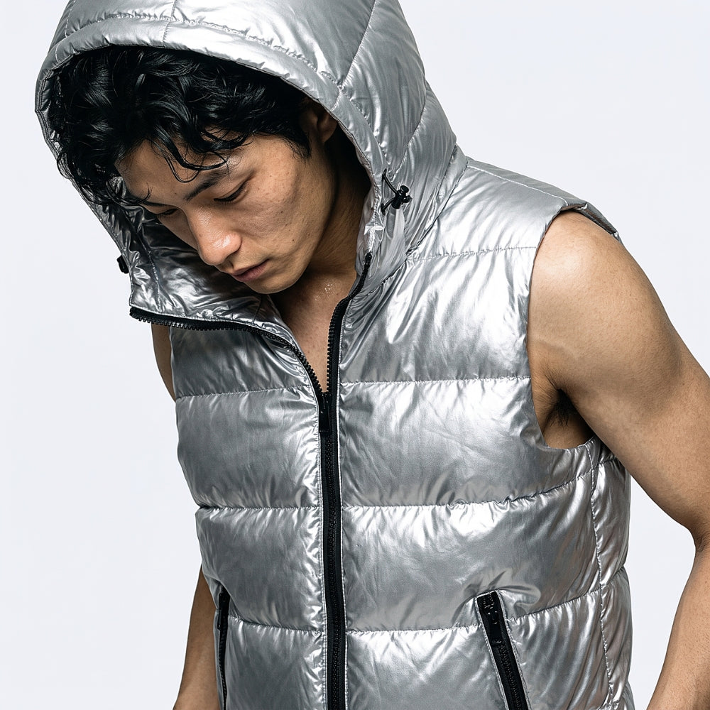 A man wearing a shiny metallic silver hooded sleeveless puffer vest with a front zipper, photographed against a light gray studio background.